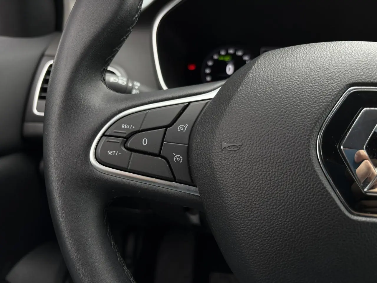 Gros plan sur le volant noir de la Renault Mégane Break 2024 avec commandes de régulateur et logo Renault central.