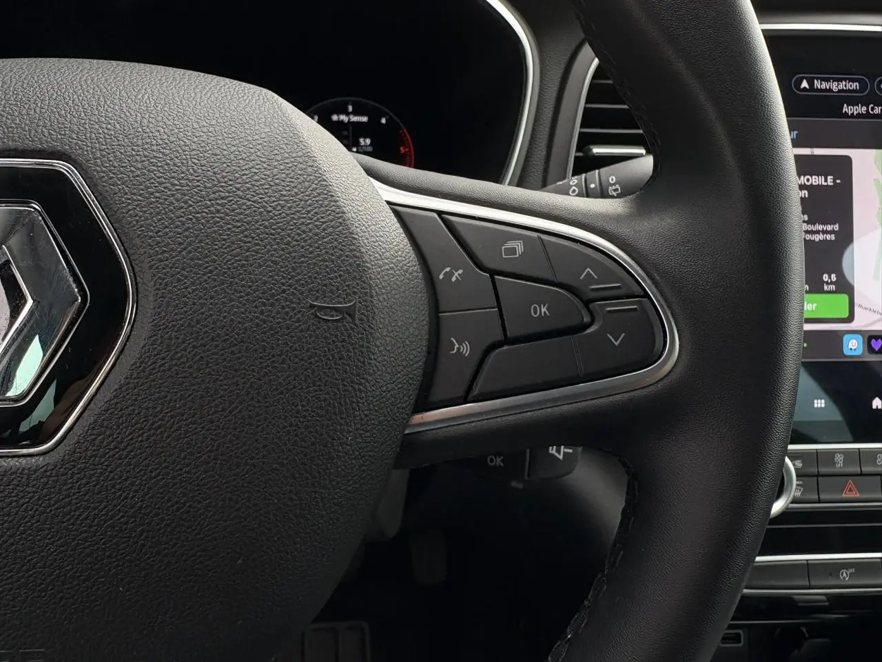 Gros plan sur le volant en similicuir noir de la Renault Mégane Break 2024 avec commandes multifonctions et écran tactile GPS visible.