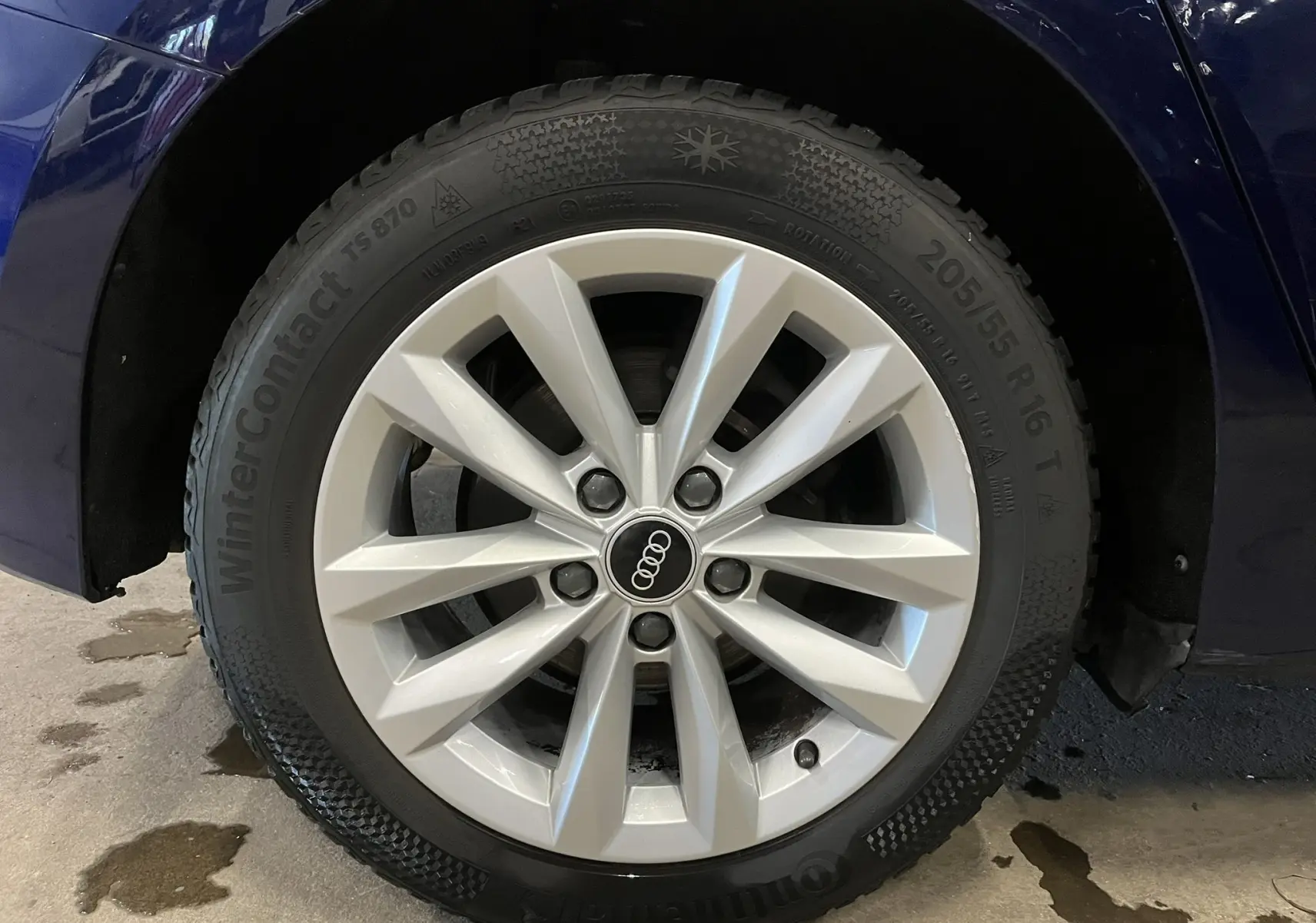 Gros plan sur la roue avant gauche d’une Audi A3 Sportback bleu métallisé avec jante argentée et pneu hiver Continental.