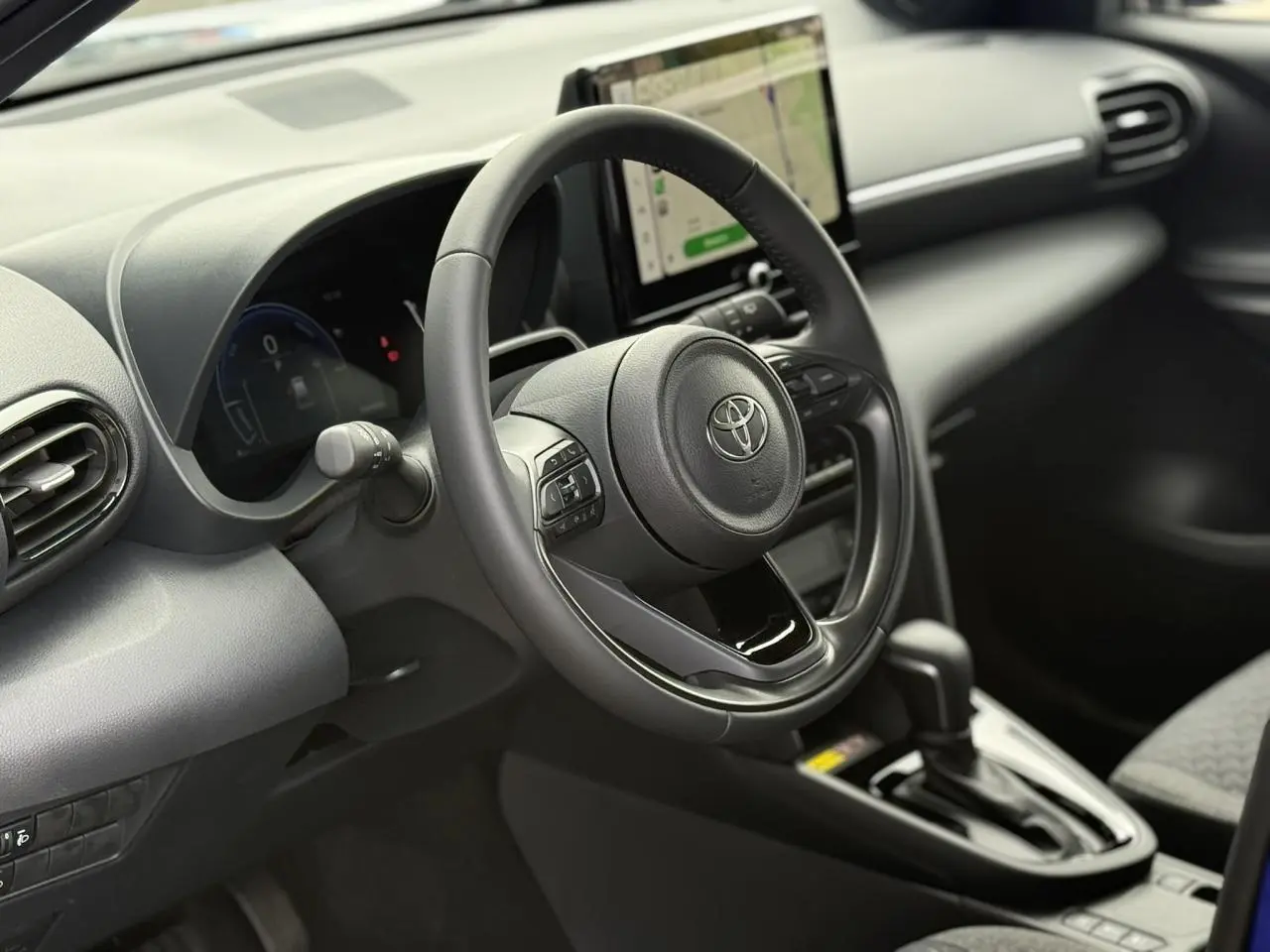 Vue intérieure centrée sur le volant cuir et l’écran tactile du tableau de bord de la Toyota Yaris Cross 2026.