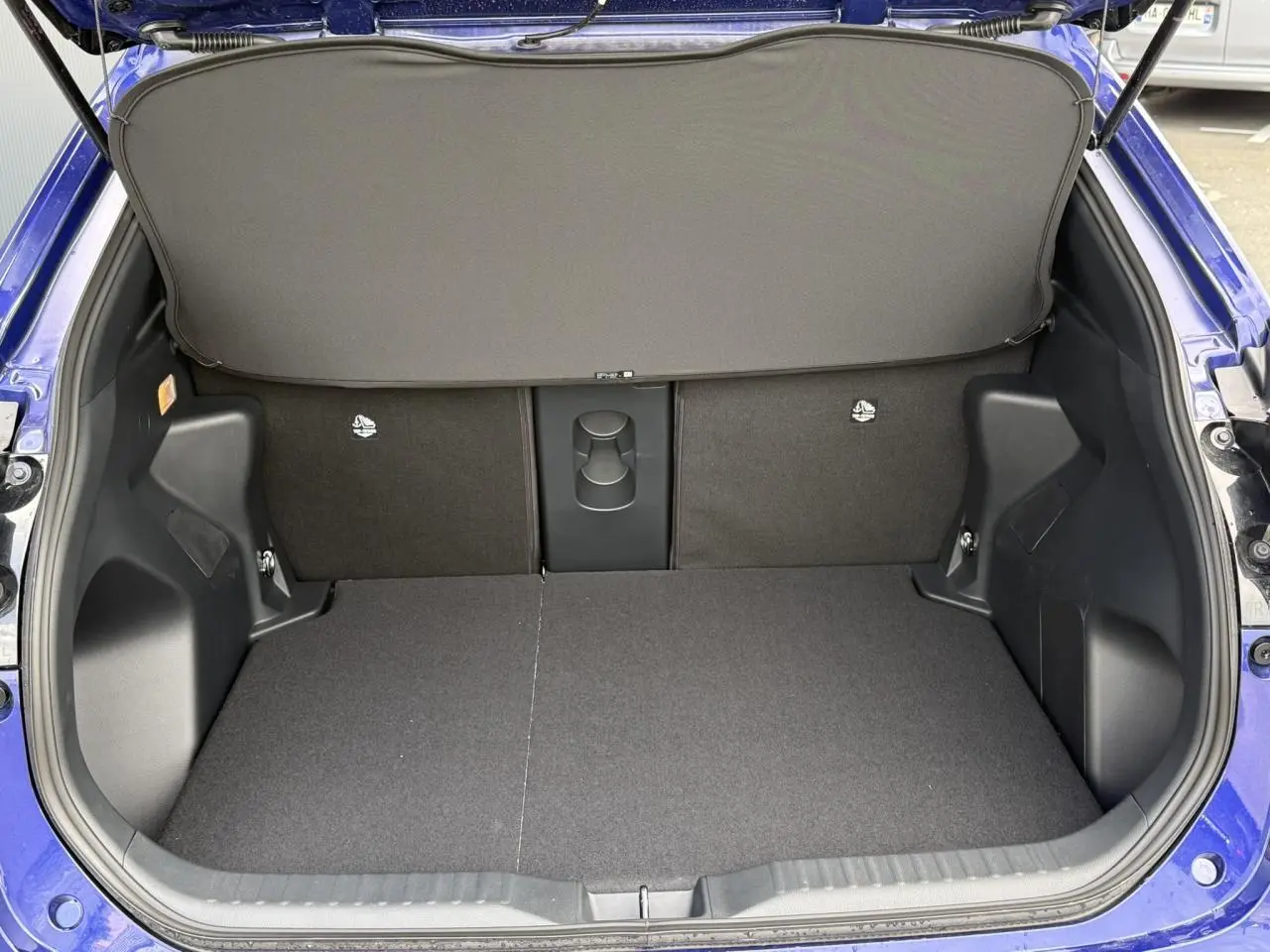 Vue arrière du coffre ouvert du Toyota Yaris Cross bleu Genievre, montrant un plancher plat et une tablette de séparation.