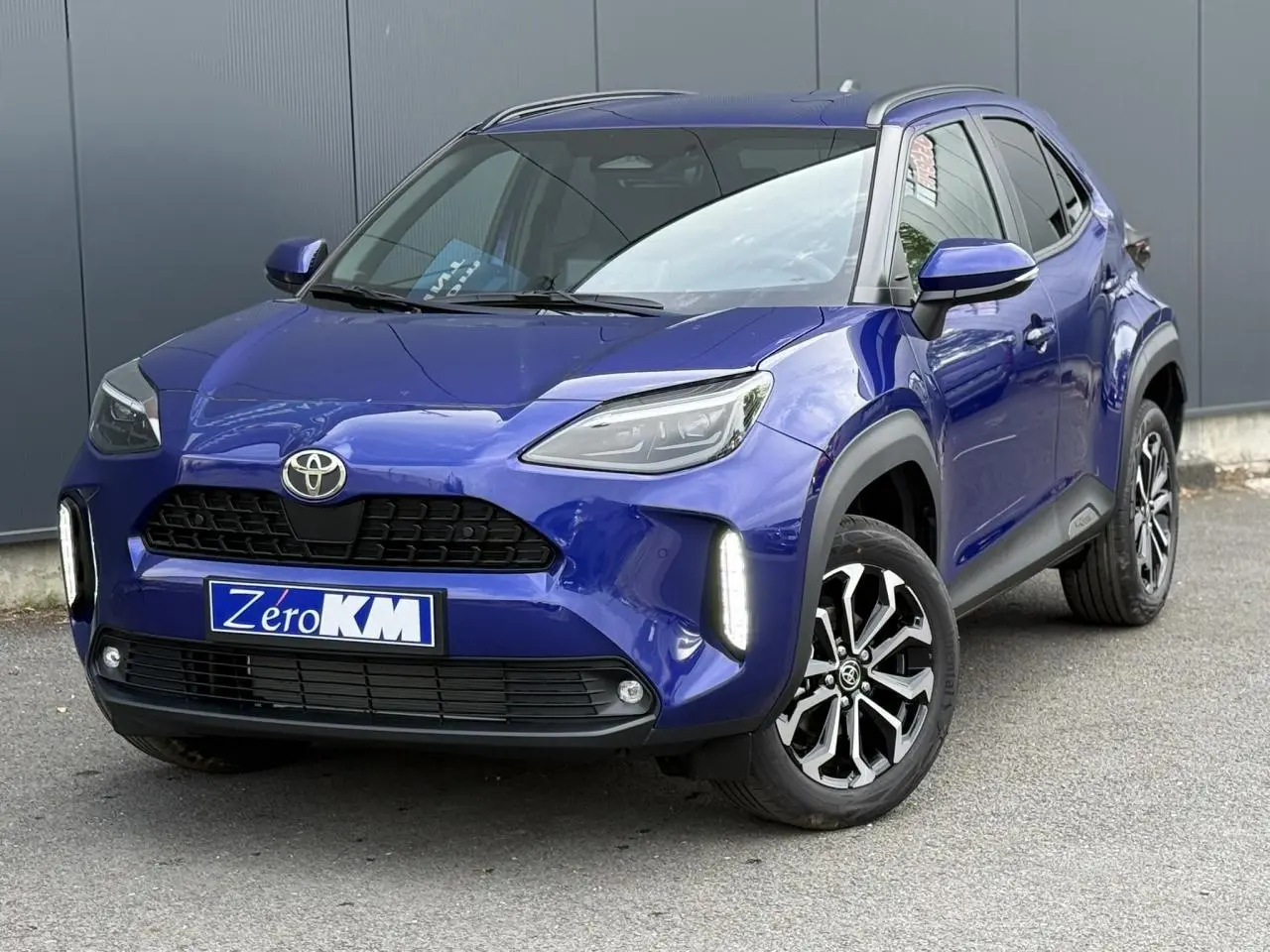 Toyota Yaris Cross bleu Genievre vue 3/4 avant droit avec feux LED verticaux allumés et jantes alliage noires.