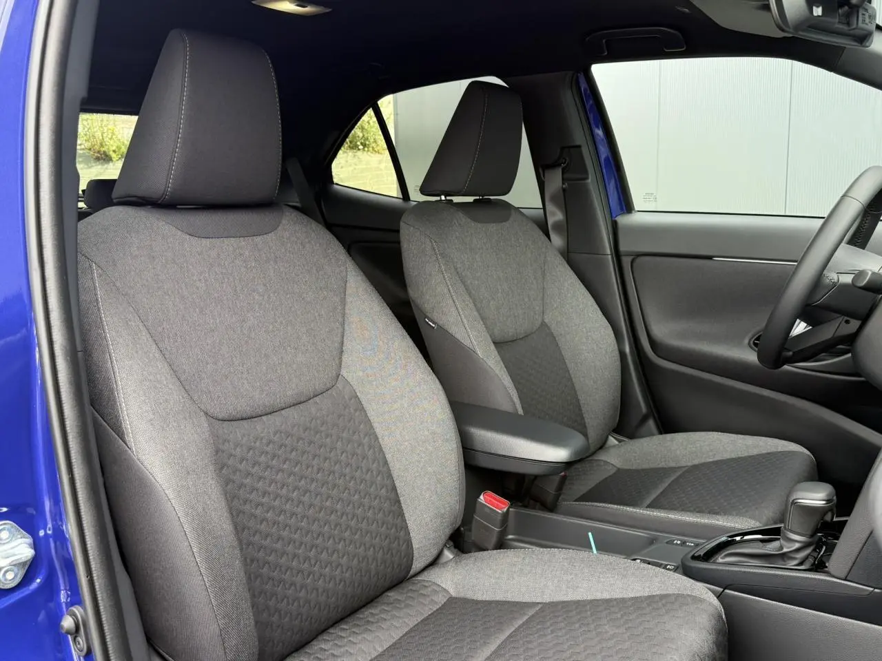 Vue intérieure côté conducteur et passager avant de la Toyota Yaris Cross bleu Genievre, sièges tissu gris et accoudoir central.