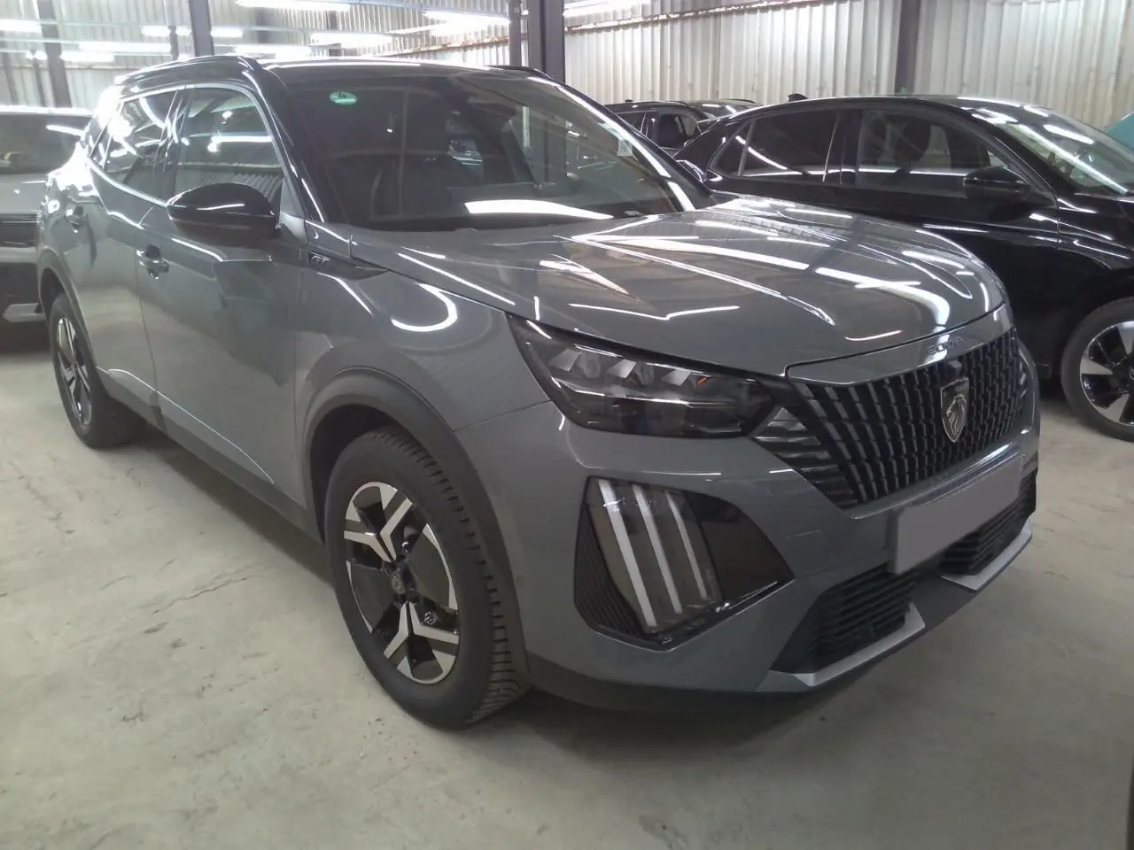 Peugeot 2008 1.2 Hybrid 145ch GT gris selenium en 3/4 avant avec barres de toit noires et calandre distinctive.