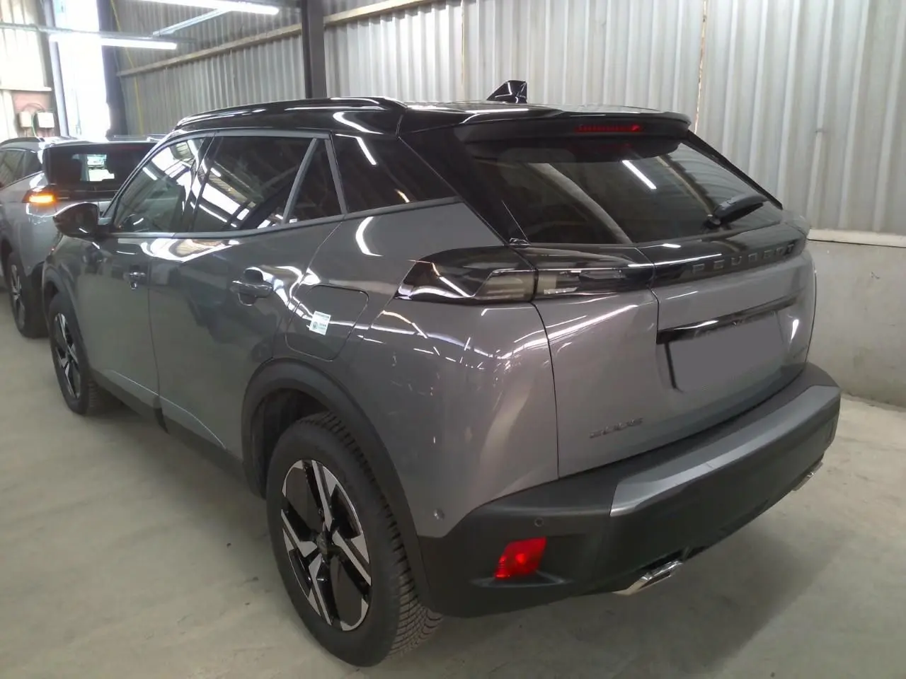 Peugeot 2008 gris selenium vue 3/4 arrière droit avec barres de toit noires dans un garage.
