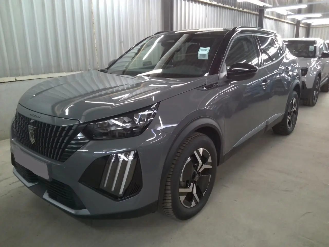 Peugeot 2008 1.2 Hybrid 145ch GT gris selenium en 3/4 avant droit avec barres de toit noires visibles.