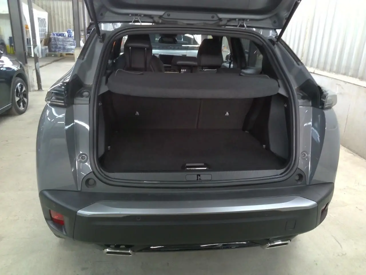 Vue arrière ouverte du coffre d'un Peugeot 2008 gris selenium, soulignant l'espace de chargement et les feux arrière.