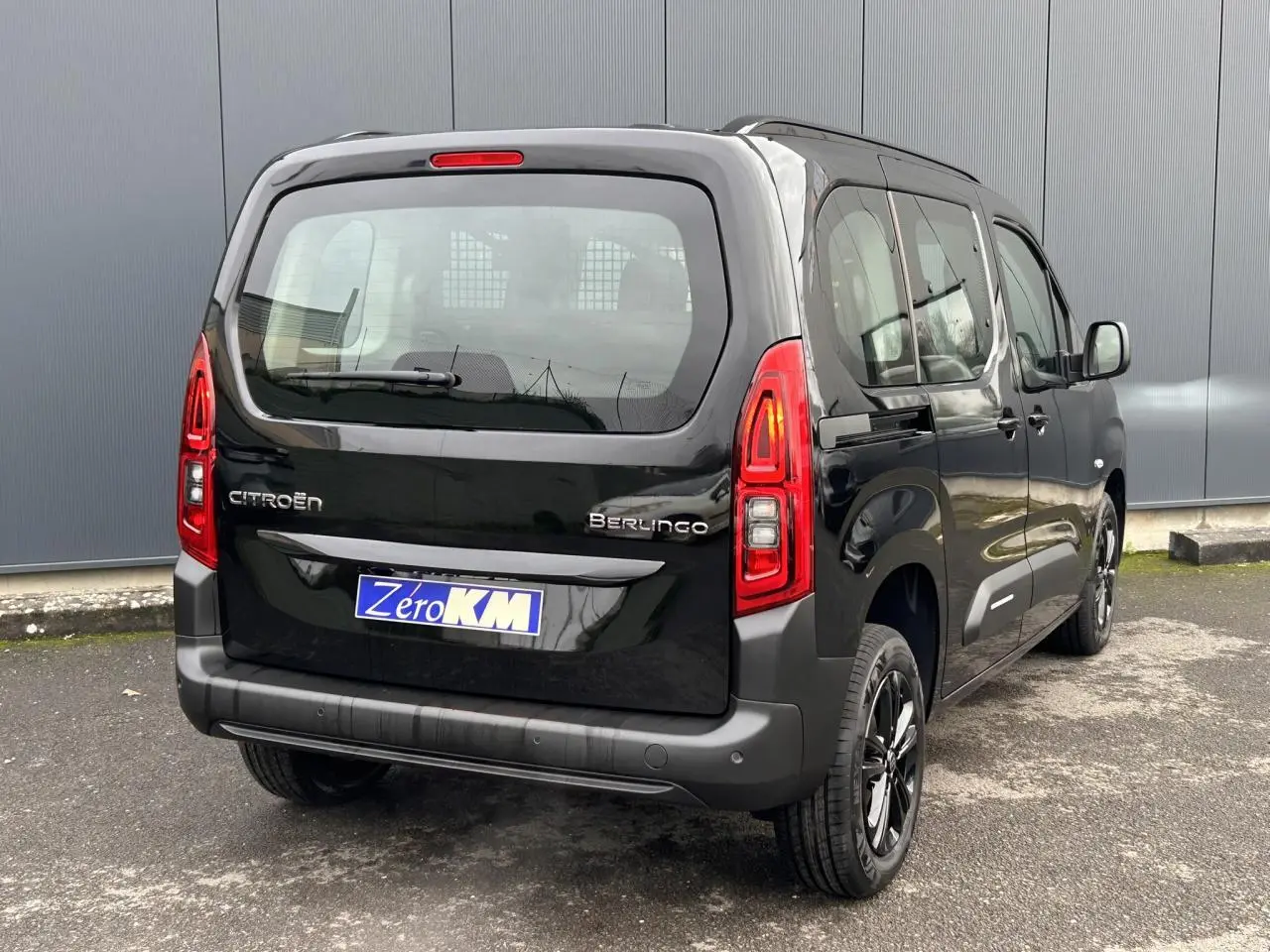 Vue 3/4 arrière droite d'un Citroën Berlingo Multispace noir Perla avec jantes alliage noires et feux arrière allumés.