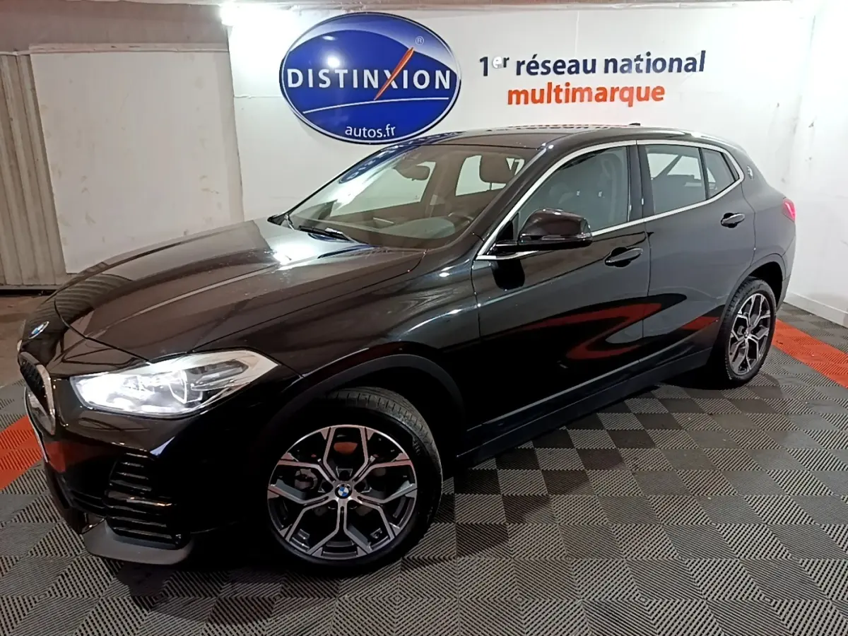 BMW X2 sDrive18i Lounge noir en 3/4 avant droit, avec jantes alliage et phares LED allumés.