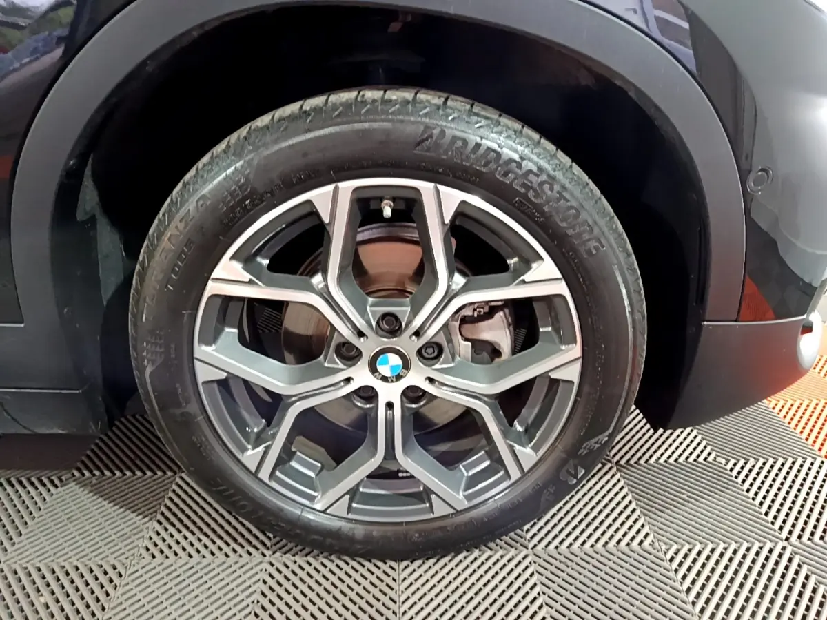 Gros plan sur la roue avant gauche noire d’un BMW X2 sDrive18i Lounge 2023 avec jante alliage distinctive.