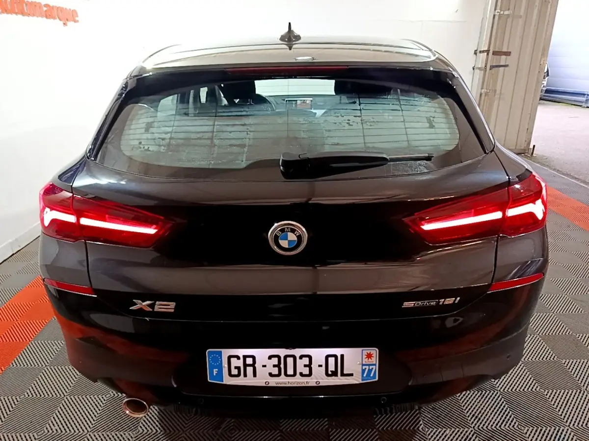 Vue arrière d'une BMW X2 sDrive18i noire avec feux LED allumés et plaque d'immatriculation française.
