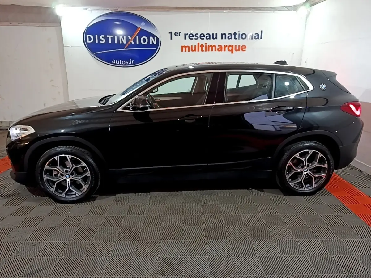 BMW X2 sDrive18i Lounge noir vue de profil côté gauche, avec jantes alliage et logo BMW sur l'aile arrière.