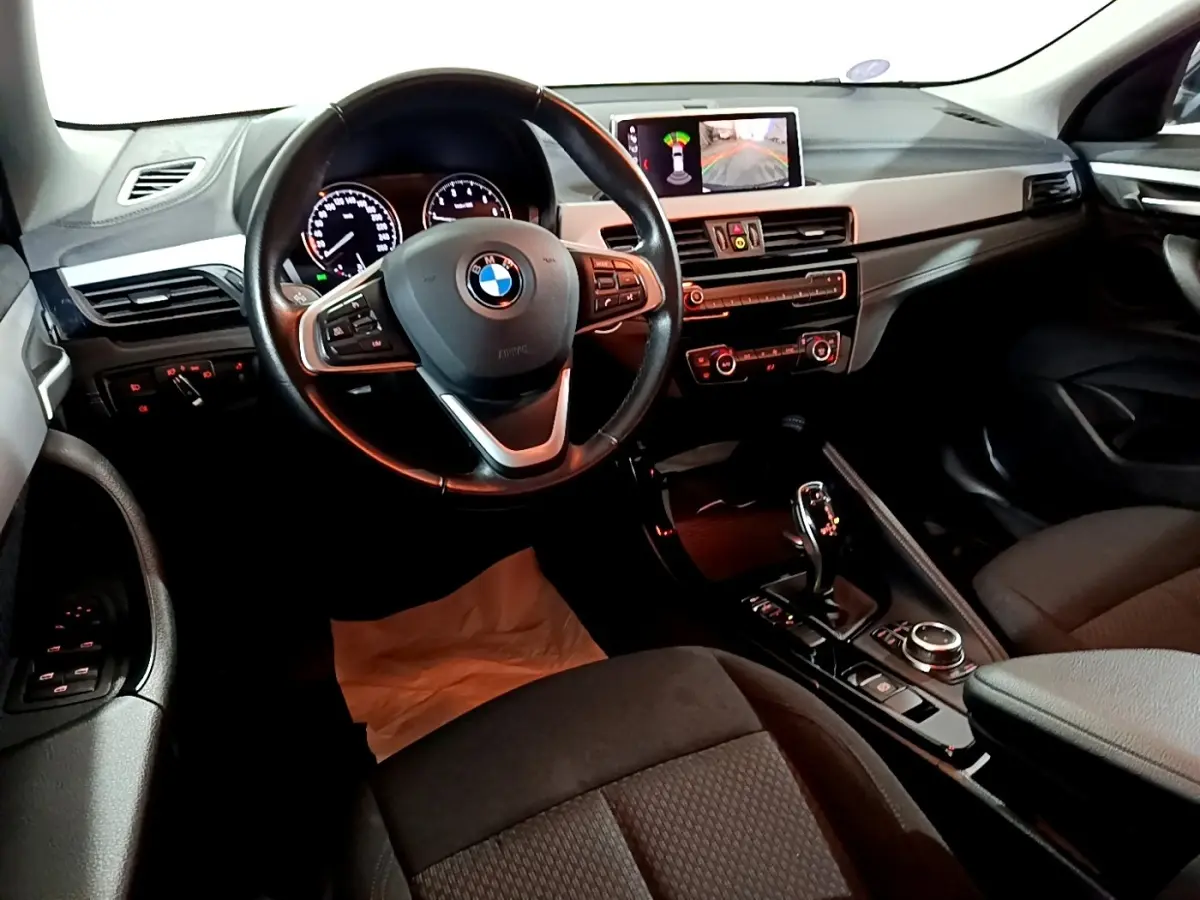 Vue intérieure avant du BMW X2 sDrive18i Lounge 2023, tableau de bord avec écran central et volant cuir multifonctions.