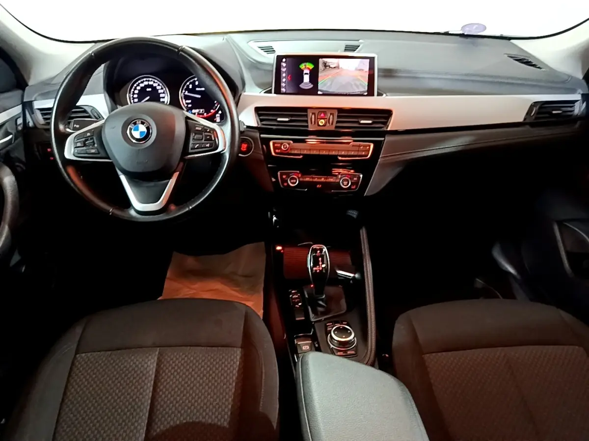 Vue intérieure avant du BMW X2 sDrive18i Lounge 2023 avec tableau de bord noir et écran central affichant l'aide au stationnement.