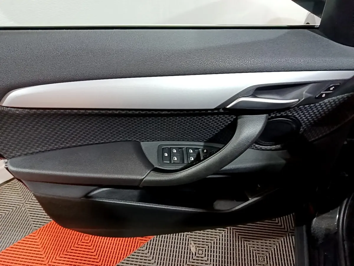 Détail de la porte côté conducteur de la BMW X2 noire 2023 avec commandes des vitres et poignée argentée.