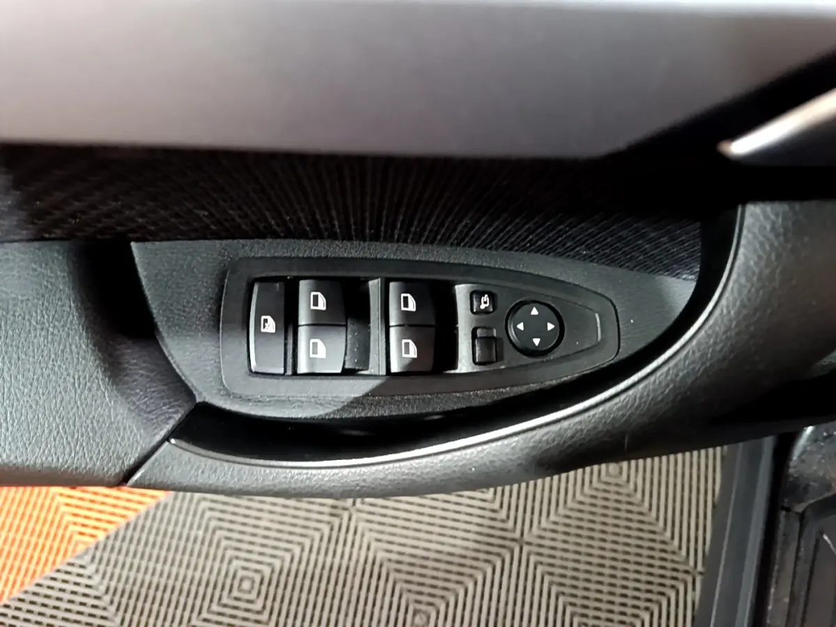 Gros plan sur les commandes de lève-vitres et rétroviseurs côté conducteur d'une BMW X2 noire.