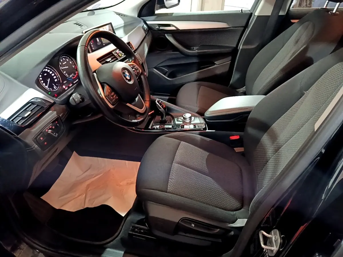 Vue intérieure côté conducteur de la BMW X2 noire 2023, montrant le volant cuir, tableau de bord digital et sièges tissu noirs.