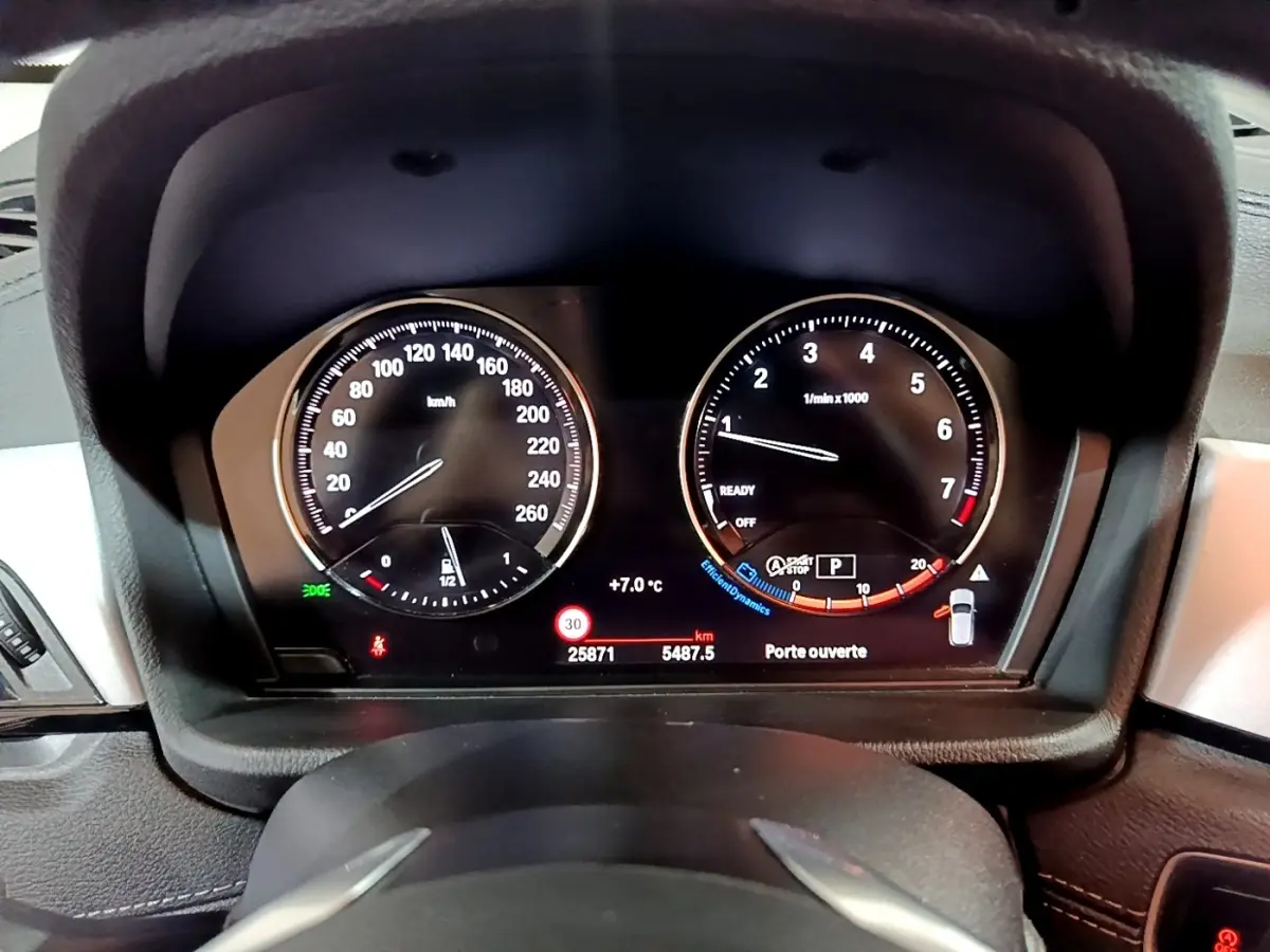 Vue rapprochée du tableau de bord numérique de la BMW X2 sDrive18i 2023, affichant vitesse, compte-tours et alertes.