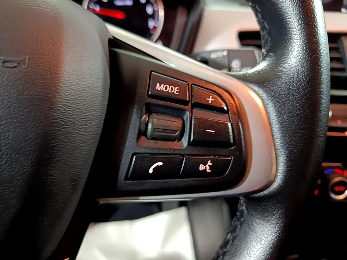 Gros plan sur les commandes gauche du volant cuir noir de la BMW X2 sDrive18i 2023, avec boutons mode et volume.