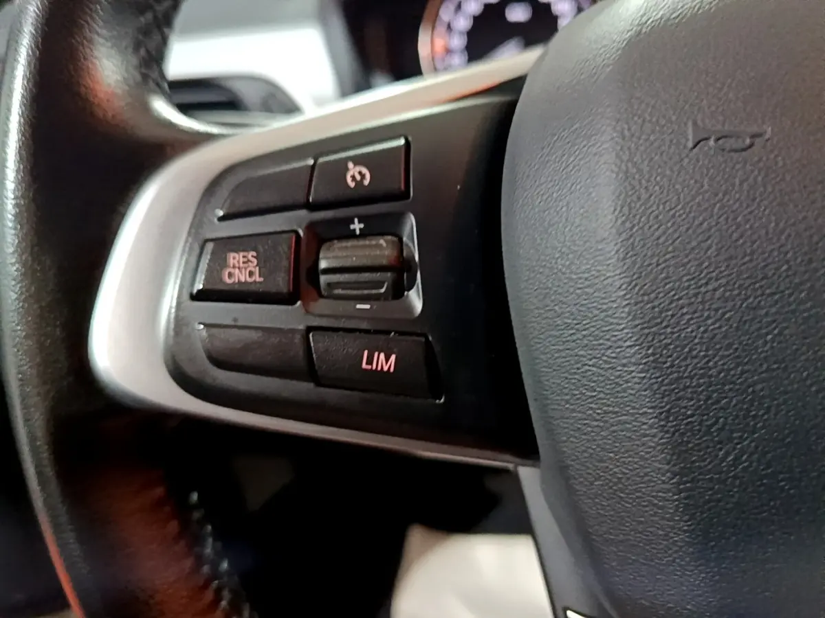 Gros plan sur les commandes de régulateur de vitesse au volant cuir noir de la BMW X2 sDrive18i Lounge 2023.