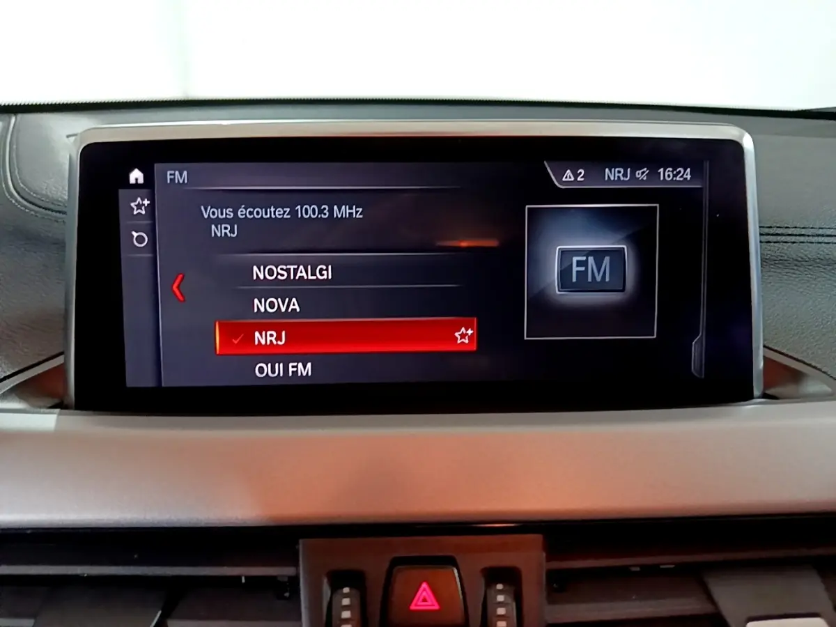 Écran central du tableau de bord du BMW X2 sDrive18i Lounge 2023 affichant la sélection radio FM NRJ.
