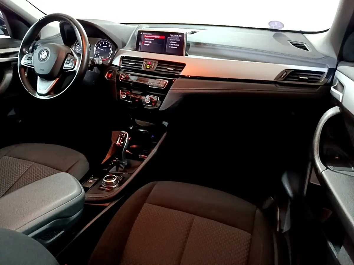 Vue intérieure côté conducteur du BMW X2 sDrive18i Lounge 2023, tableau de bord noir avec écran central et volant cuir.