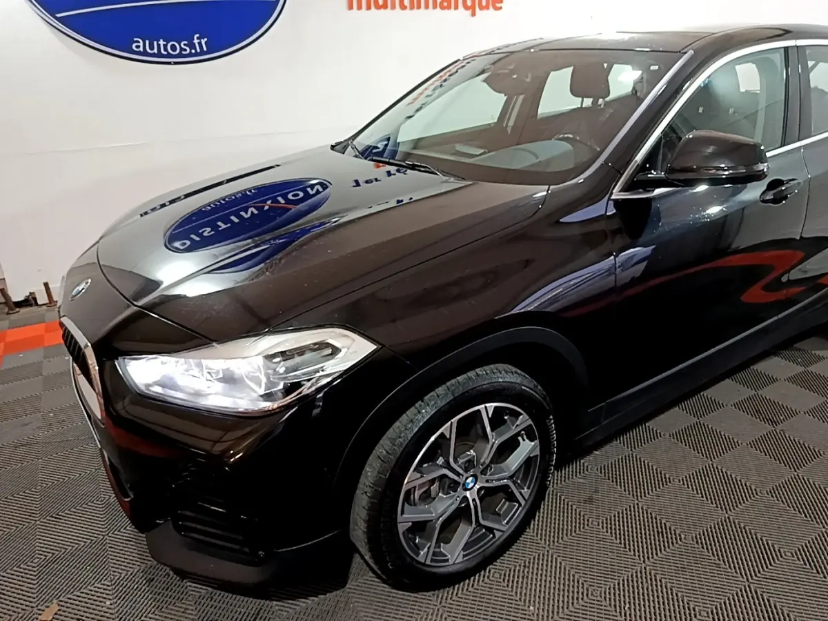 Vue 3/4 avant droit d'un BMW X2 noir 2023 avec phares LED allumés et jantes alliage distinctives.