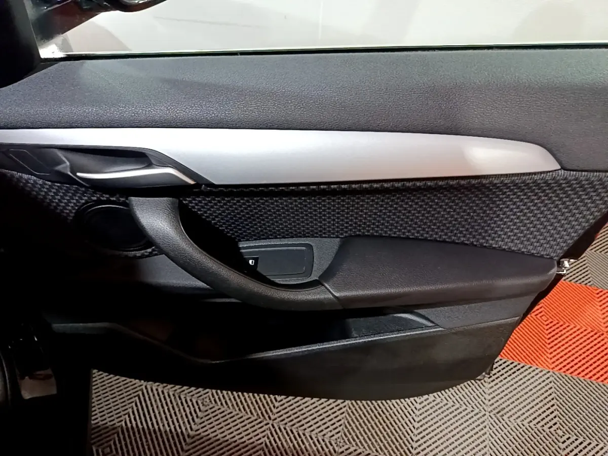Gros plan sur la porte côté gauche noire avec insert texturé et poignée intérieure argentée du BMW X2 sDrive18i 2023.