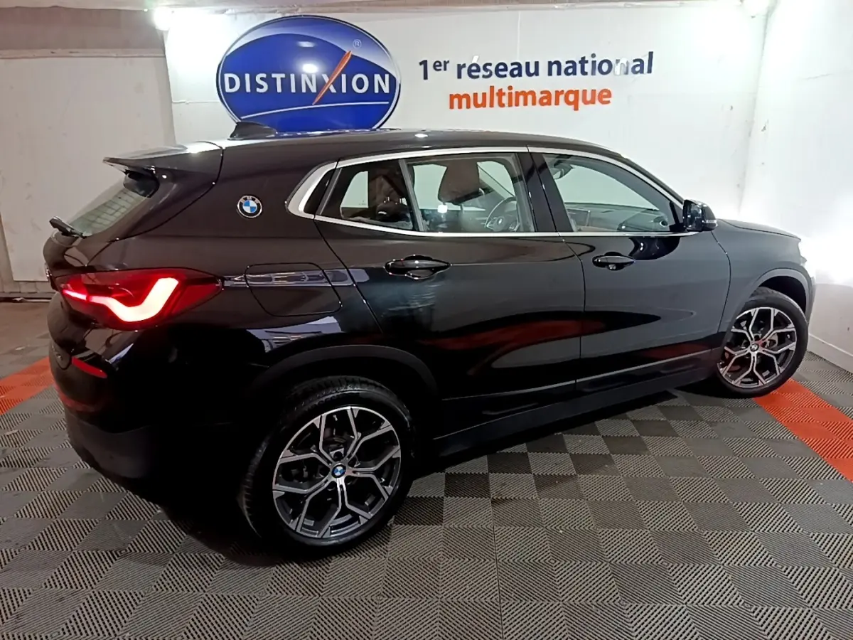 BMW X2 sDrive18i noir en vue de profil côté gauche, avec feux arrière allumés et jantes alliage distinctives.