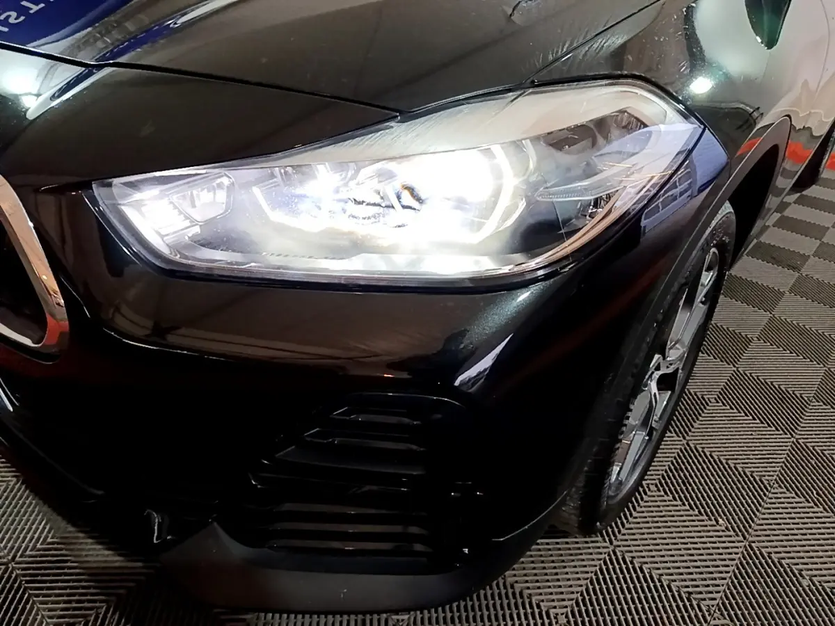 Gros plan sur l'avant droit noir brillant du BMW X2 2023 avec phare LED allumé et jante visible.