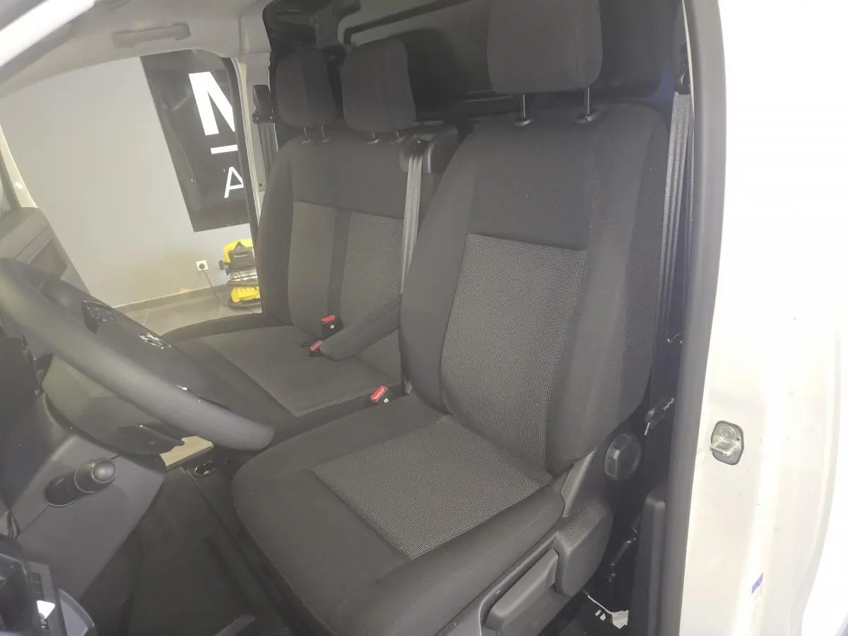 Vue intérieure côté conducteur de l'Opel Vivaro blanc, montrant la banquette et le siège avant en tissu noir.