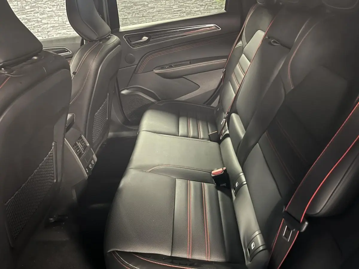 Vue latérale intérieure arrière du Renault Arkana 2023 noir avec sellerie cuir/suédine et surpiqûres rouges.