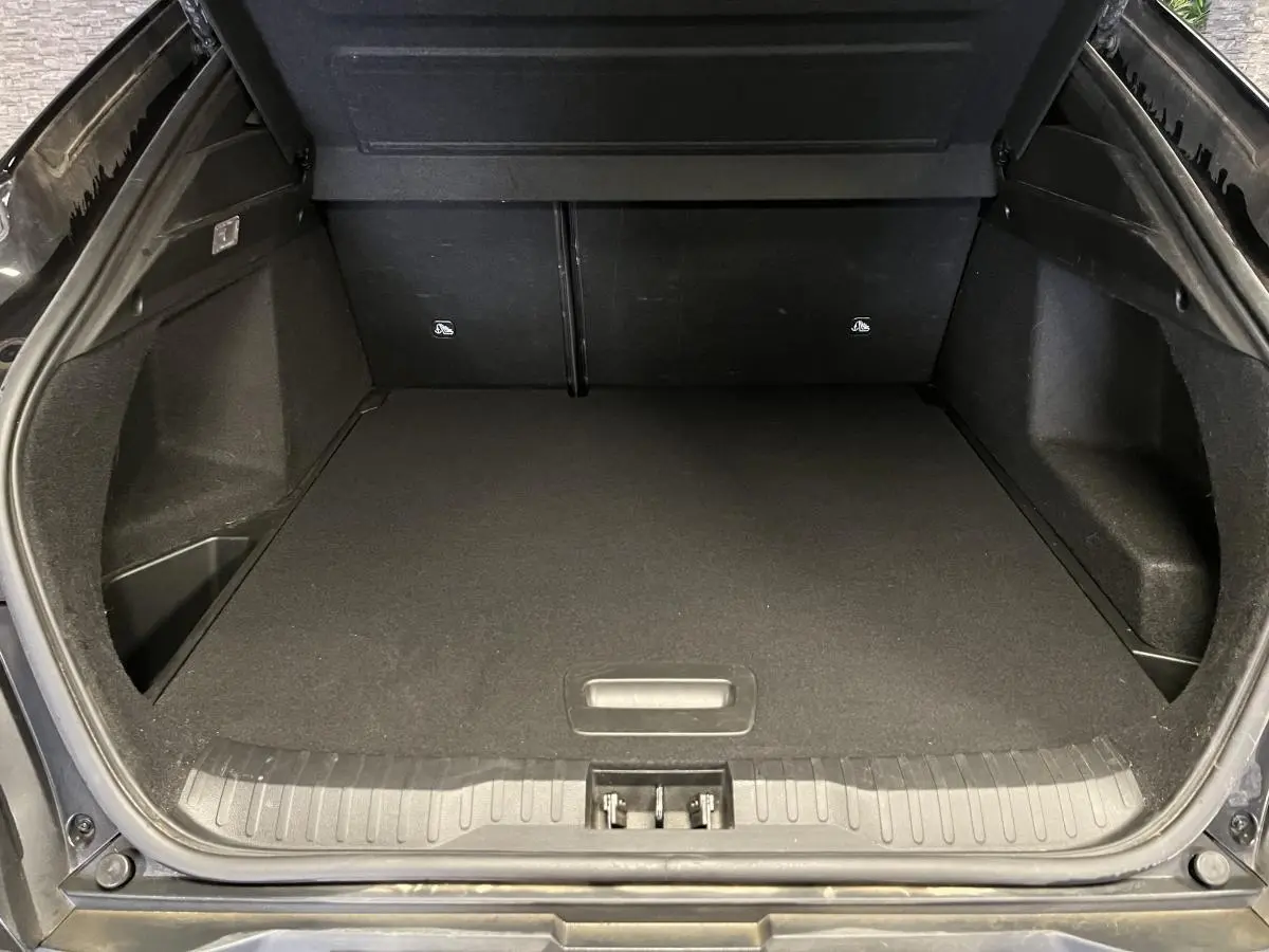 Coffre ouvert vu de l'arrière d'un Renault Arkana noir 2023, espace de chargement vide et tapis noir.