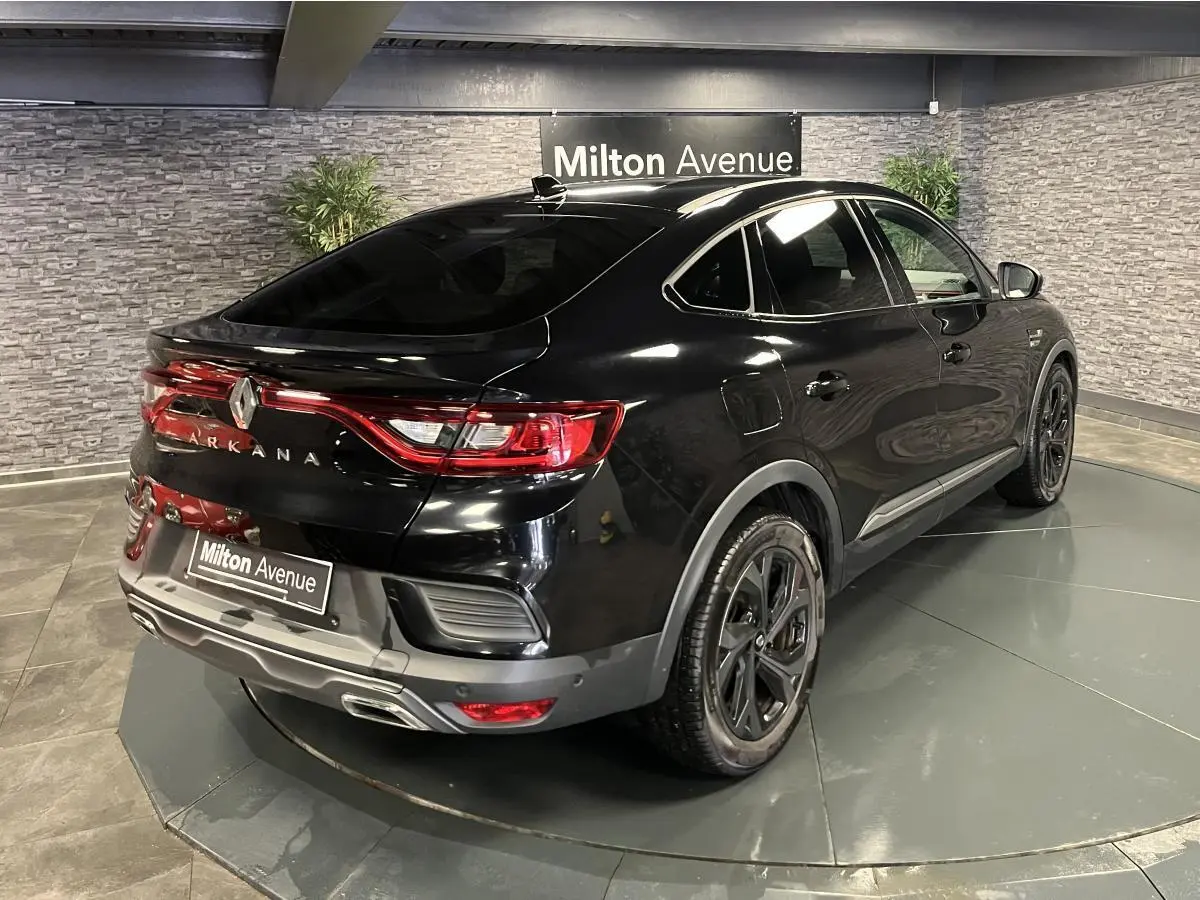 Vue 3/4 arrière droite d'un Renault Arkana noir brillant avec jantes noires et feux arrière LED allumés en intérieur showroom.