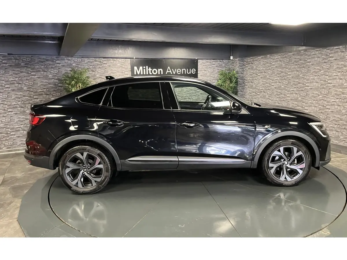 Vue de profil côté gauche d'un Renault Arkana noir métallisé avec jantes alliage et toit plongeant en intérieur showroom.