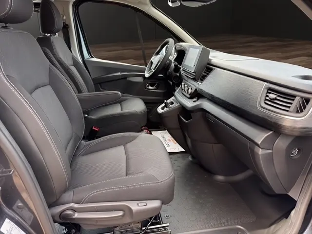 Vue intérieure côté conducteur du Renault Trafic Fourgon gris foncé, montrant les sièges avant, le volant multifonctions et l’écran tactile central.