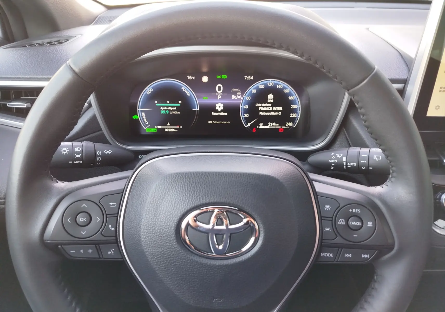 Vue centrée sur le volant noir avec logo Toyota et tableau de bord numérique du Corolla Cross gris minéral 2025.
