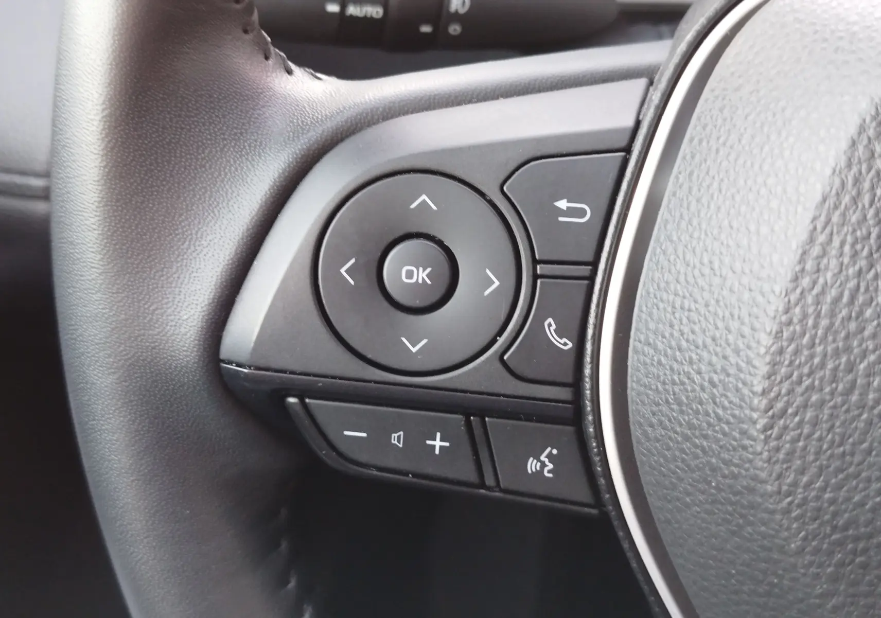 Gros plan sur les commandes gauche du volant gris du Toyota Corolla Cross 1.8 140ch Dynamic 2025, boutons multifonctions visibles.
