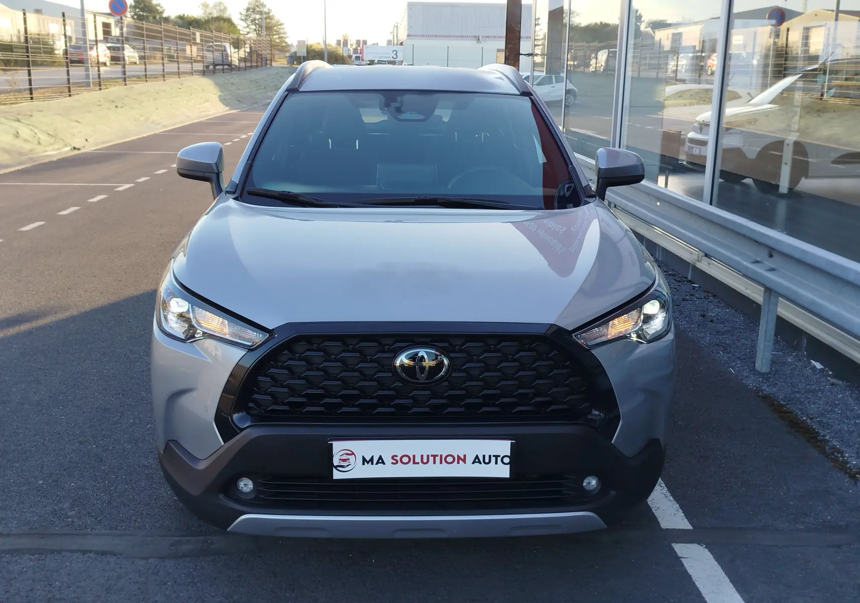 Vue avant centrée du Toyota Corolla Cross 2025 gris minéral avec calandre noire et feux LED allumés.