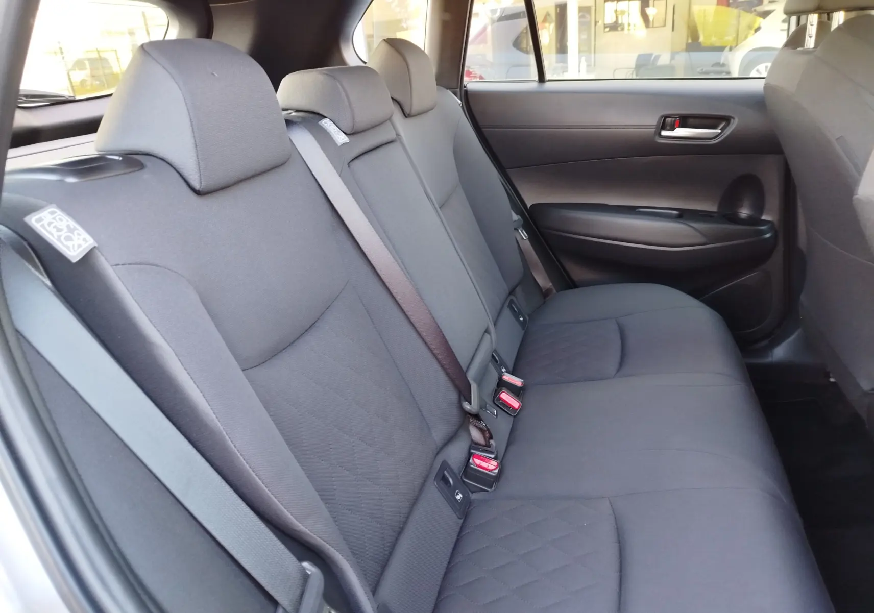 Vue intérieure côté droit des sièges arrière gris tissu de la Toyota Corolla Cross 2025, avec ceintures de sécurité visibles.