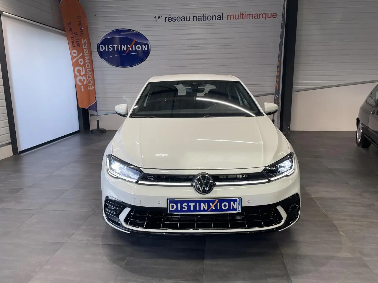 Vue avant d'une Volkswagen Polo blanche 2024 R-Line avec calandre spécifique et feux LED allumés en showroom.
