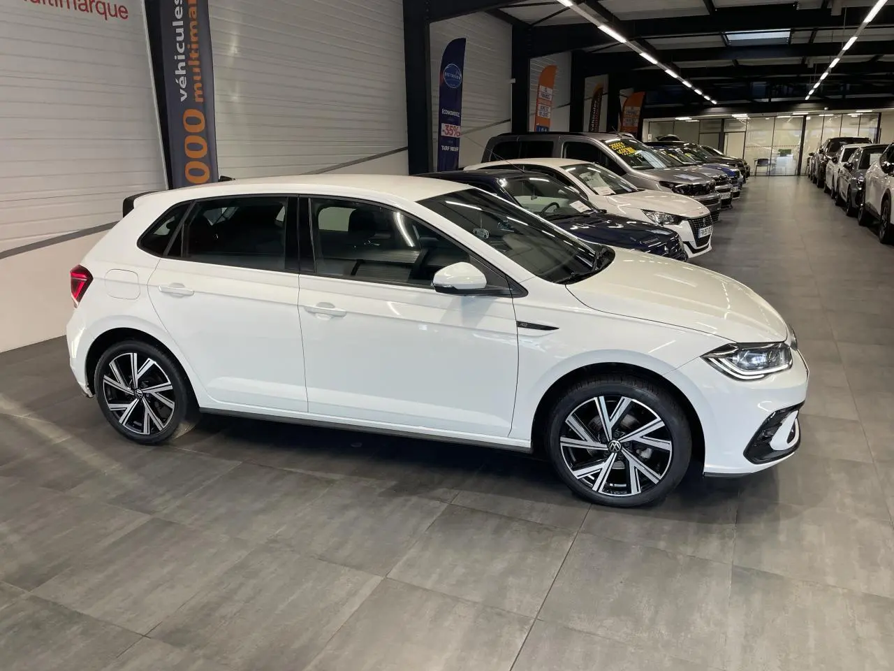 Volkswagen Polo 2024 blanche vue de profil côté gauche en intérieur avec jantes alliage R-Line visibles.