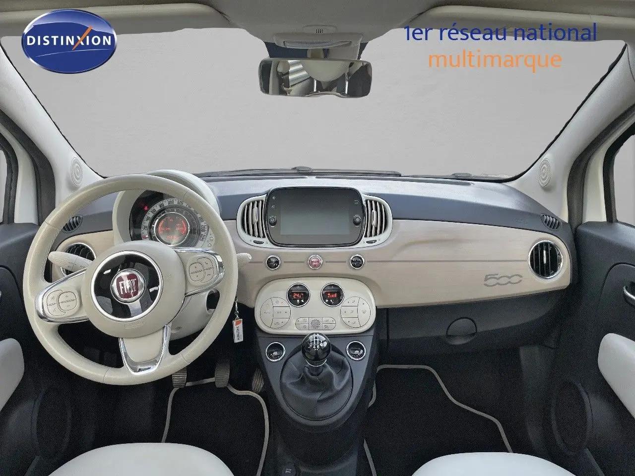 Intérieur clair de la Fiat 500 1.0 Hybrid 2022, vue frontale du tableau de bord avec volant beige et console centrale moderne.