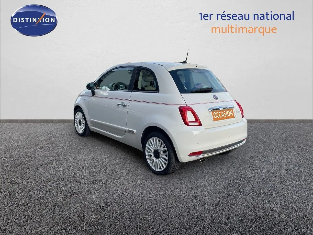 Vue 3/4 arrière gauche d'une Fiat 500 blanche 1.0 Hybrid 70CH DolceVita avec jantes biton et bande rouge décorative sur la carrosserie.