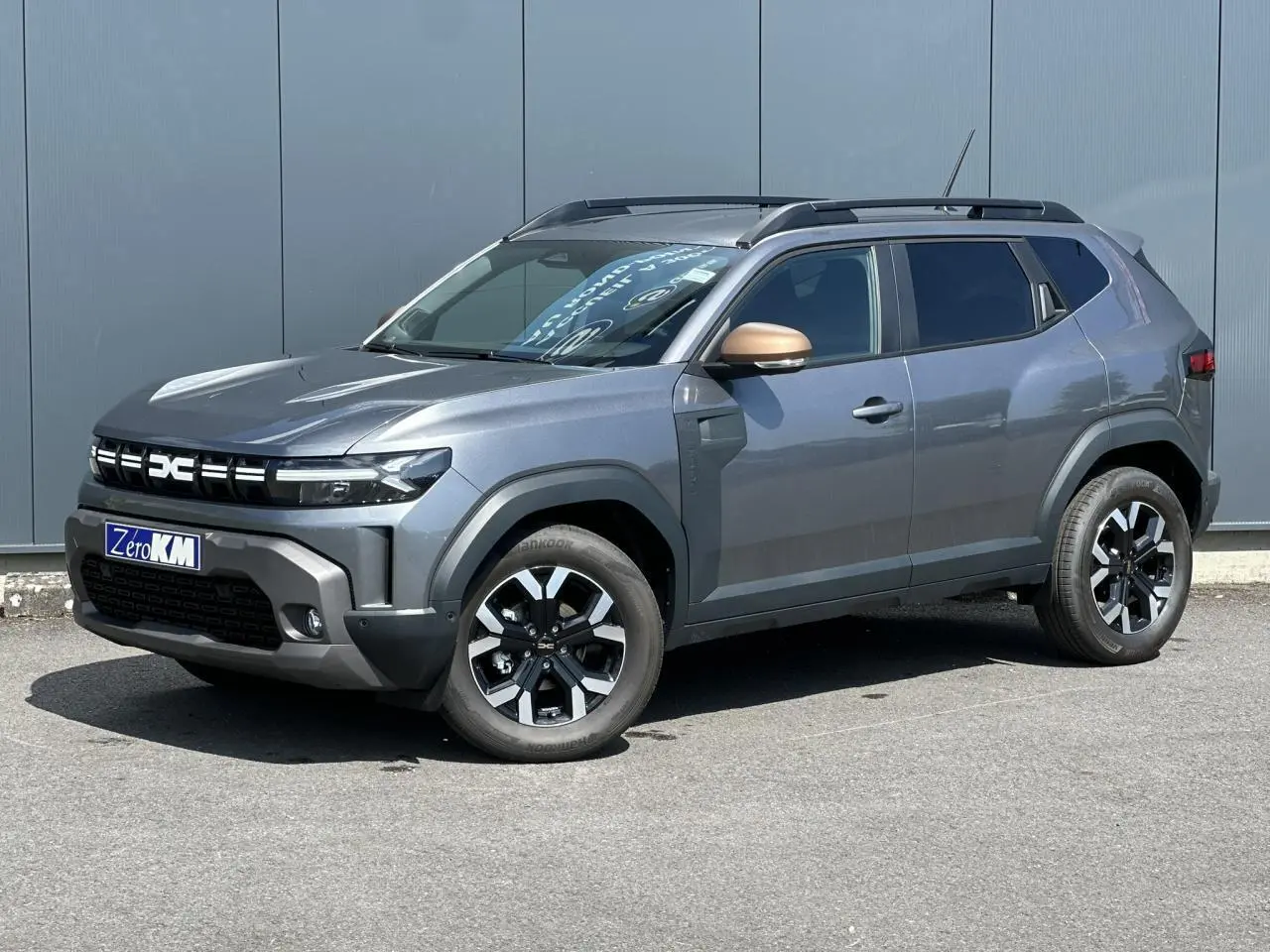 Dacia Duster ECO-G 100 gris schiste en 3/4 avant droit avec jantes alliage et barres de toit noires.