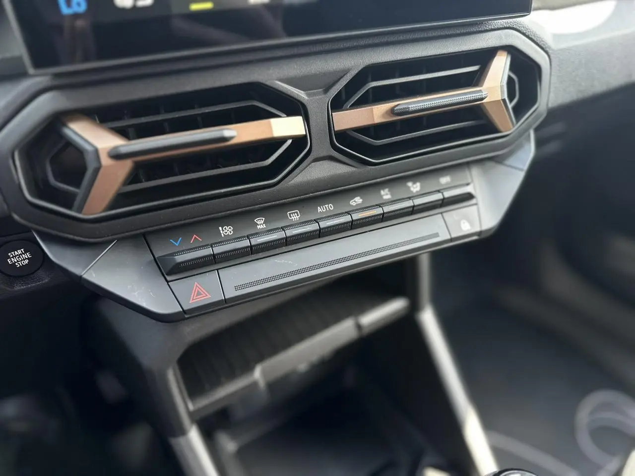 Détail de la console centrale du Dacia Duster 2025 gris, avec commandes climatisation et aérateurs hexagonaux bronze.