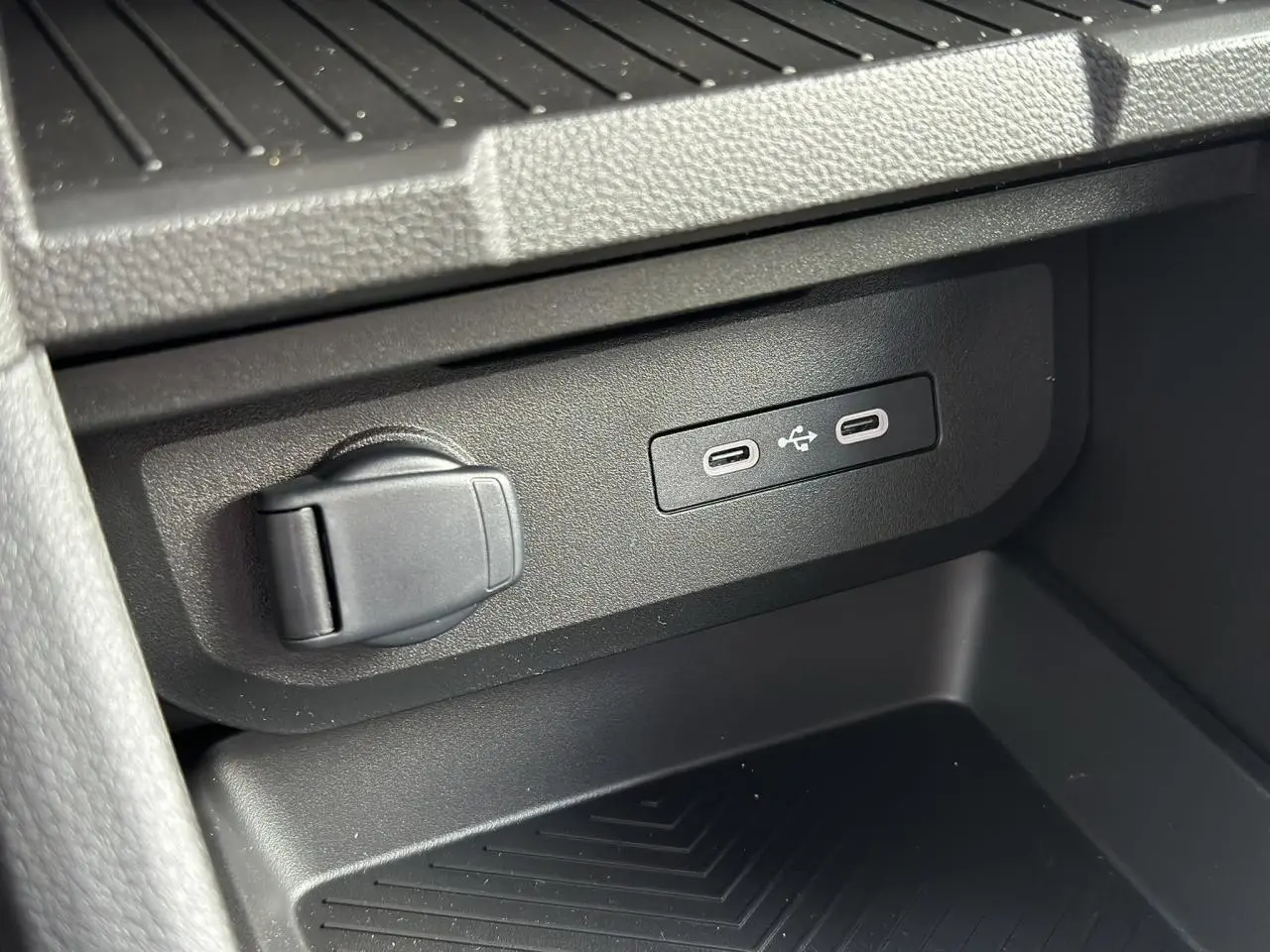 Prise USB et prise 12V noires en gros plan dans l'espace de rangement central du Dacia Duster Gris Schiste 2025.