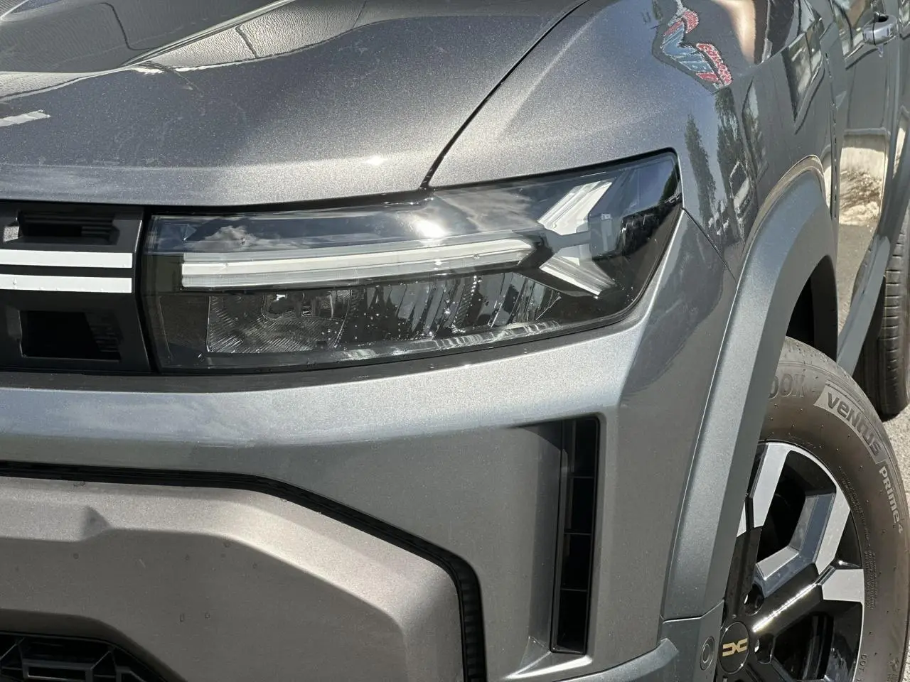 Gros plan sur le phare avant droit et la jante alliage du Dacia Duster 2025 gris schiste, version ECO-G 100 Extrême.