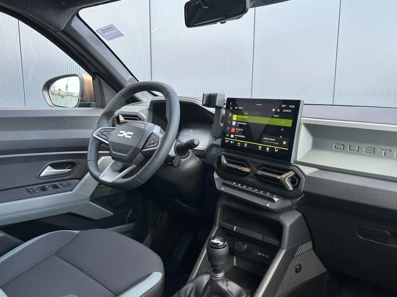 Vue intérieure côté conducteur du Dacia Duster 2025 avec tableau de bord digital et écran tactile central.