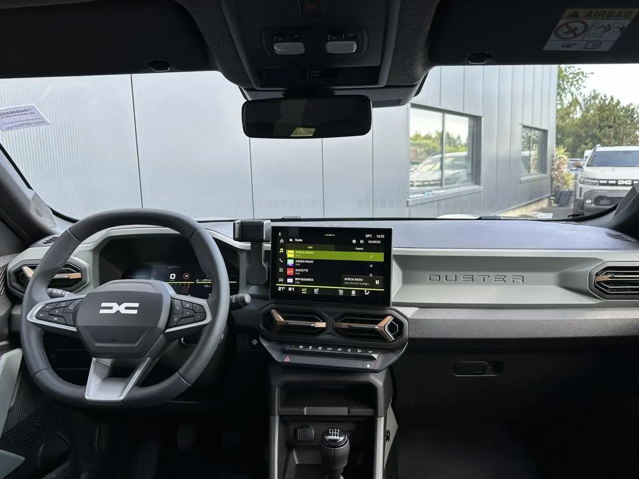 Tableau de bord du Dacia Duster 2025 gris, vue frontale du volant et écran tactile central avec commandes modernes.